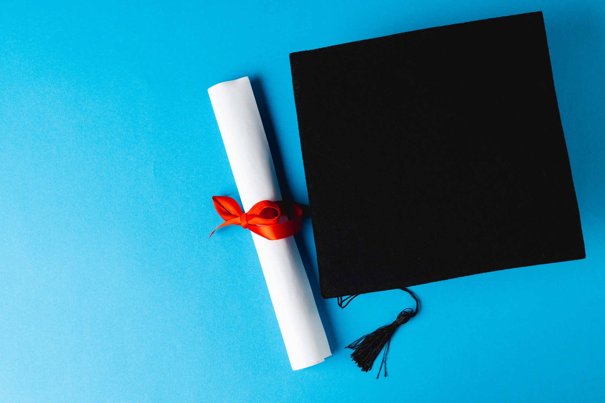 Image of graduation hat and diploma on blue surface
